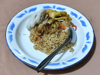 Fried rice with omelet, chicken pieces and red chili slices, has a delicious taste, served on a classic iron plate, with a brown background.