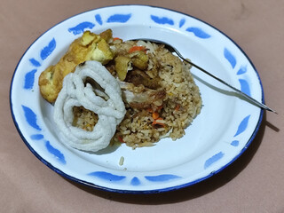 Fried rice with omelet, chicken pieces and red chili slices, has a delicious taste, served on a classic iron plate, with a brown background.