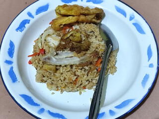 Fried rice with omelet, chicken pieces and red chili slices, has a delicious taste, served on a classic iron plate, with a brown background.