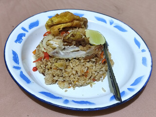Fried rice with omelet, chicken pieces and red chili slices, has a delicious taste, served on a classic iron plate, with a brown background.