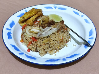 Fried rice with omelet, chicken pieces and red chili slices, has a delicious taste, served on a classic iron plate, with a brown background.