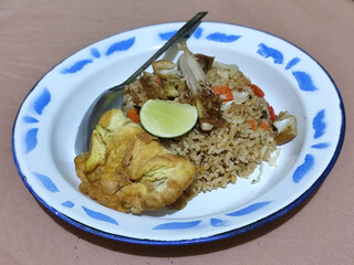 Fried rice with omelet, chicken pieces and red chili slices, has a delicious taste, served on a classic iron plate, with a brown background.