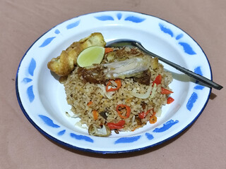 Fried rice with omelet, chicken pieces and red chili slices, has a delicious taste, served on a classic iron plate, with a brown background.