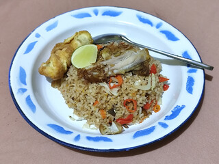Fried rice with omelet, chicken pieces and red chili slices, has a delicious taste, served on a classic iron plate, with a brown background.