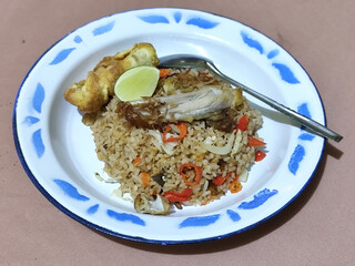 Fried rice with omelet, chicken pieces and red chili slices, has a delicious taste, served on a classic iron plate, with a brown background.