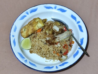 Fried rice with omelet, chicken pieces and red chili slices, has a delicious taste, served on a classic iron plate, with a brown background.