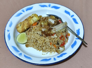 Fried rice with omelet, chicken pieces and red chili slices, has a delicious taste, served on a classic iron plate, with a brown background.