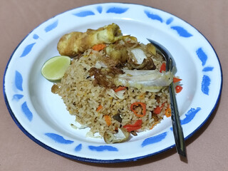 Fried rice with omelet, chicken pieces and red chili slices, has a delicious taste, served on a classic iron plate, with a brown background.