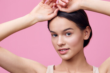 Young woman with clear skin and a natural pose against a pink background, expressing confidence and...