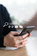 Close-up of a hand holding a smartphone with contact us icons, showing email, phone, chat, and communication options for customer service or business support on mobile.