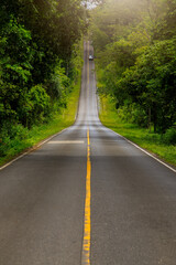 A paved road passing through dense forest with mountains in the background at Khao Yai National...