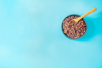 Top-right bowl of dried Sichuan peppercorn husks with tiny wooden spoon on vivid sky-blue background, minimal culinary flat-lay with large copy space