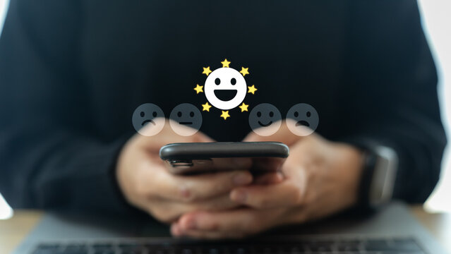 Hand holding smartphone with five-star happy emoji icon, representing excellent customer satisfaction, positive review, user feedback, rating system, and quality service concept.