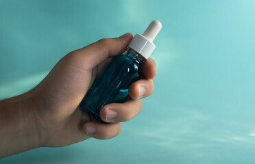 Mano sosteniendo una botella de gotero azul sobre fondo azul acuático