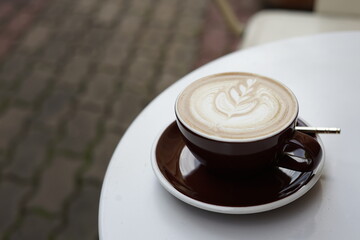 A cup of coffee with a white foam on top sits on a white table