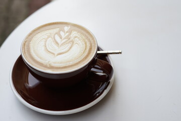 A cup of coffee with a leaf design on top sits on a white table