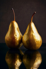 Golden pears with reflection below, dark background, beautifully balanced lighting.