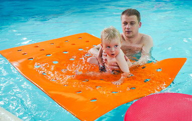 A man is holding a baby on a pool float