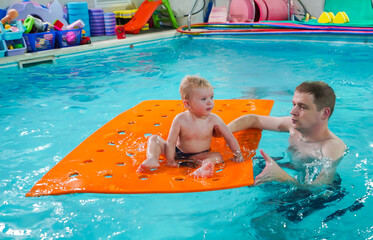 A man is holding a baby on a pool float
