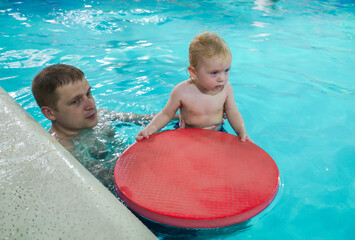 A man is holding a baby in a pool