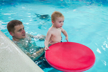 A man is holding a baby in a pool