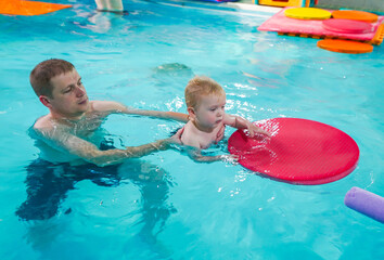 A man is holding a baby in a pool
