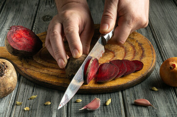 A person skillfully slices vibrant red beets with a sharp knife on a wooden cutting board....