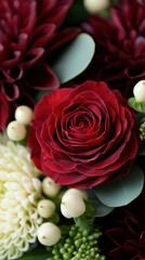 A close-up of a vibrant red rose surrounded by white berries, green foliage, and dark red flowers, showcasing a rich and elegant floral arrangement.