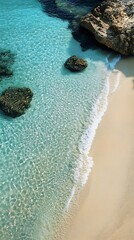 Turquoise water meets sandy shore with rocks, creating a serene and tropical beach scene