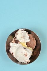 top-down view shows a metal bowl filled with scoops of assorted ice cream flavors against a light blue background