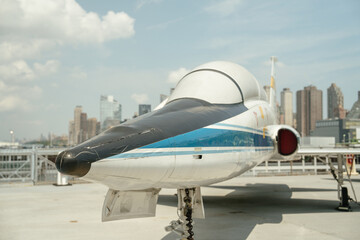Front view of aircraft nose and cockpit area with urban buildings in the background. The plane's...