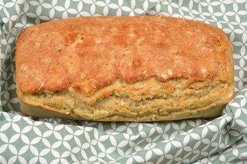 A golden-brown loaf of homemade bread is placed on a green and white patterned fabric