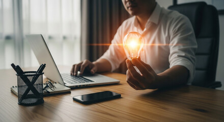 Innovation idea concept, man holding light bulb, working on laptop, symbol of digital inspiration.