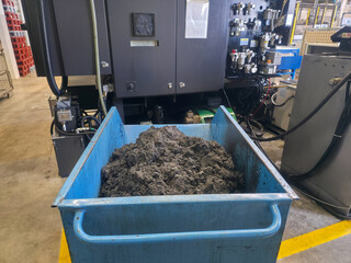 Industrial machinery working with a blue container filled with gray material in a factory setting