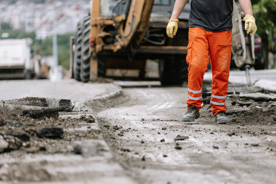 Construction worker repairs the street in urban area during daylight hours with heavy machinery nearby