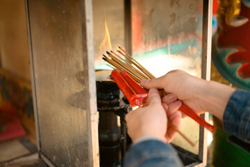 Close-up of hands lighting incense sticks and a red candle at a traditional shrine flame