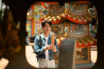 Spiritual moment as a tourist pauses to pray with incense and a candle at an ornate Chinese shrine