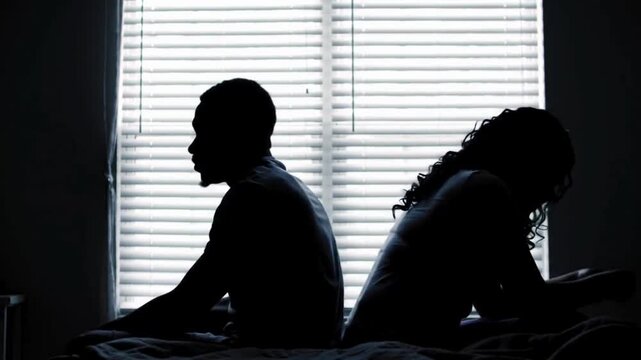 A couple quarreling concept of family relationship problems divorce, black silhouette of man and woman sitting at bed back to back resentment towards each other window in dark room
