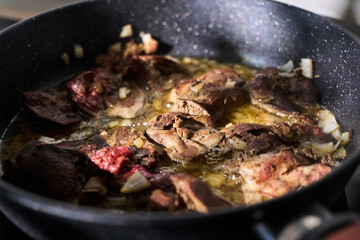 Cooking liver pieces in a frying pan with steam rising and kitchen appliances in the background