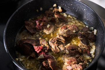 Cooking sliced liver with onions in a frying pan on a stovetop, showcasing the preparation of a hearty dish at home