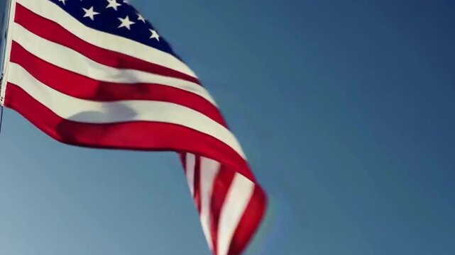 Slow motion footage of the American flag fluttering gently in the wind against a clear blue sky, cinematic lighting, seamless loop for patriotic mood