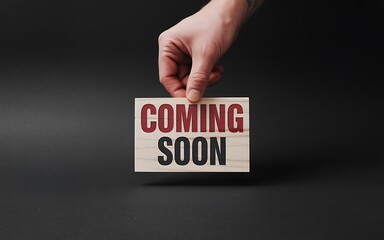 Hand holding wooden sign with coming soon text image