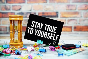 Stay True To Yourself text on paper card with hourglass and stationary on wooden background