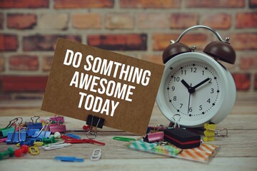Do Somthing Awesome Today text on paper card with alarm clock and stationary on wooden background