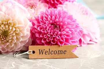 Welcome card and dahlia flowers on grey marble table, closeup