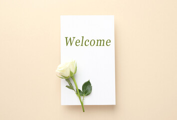 Welcome card and rose on beige background, top view