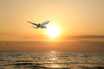 Airplane flying above sea in beautiful sky with clouds at sunset