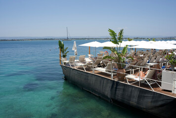 Scenic waterfront view of a stylish lounge area on a boat with sun loungers and tropical plants by...