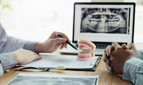 Dentist reviewing dental x-ray on computer screen. A dentist inspects a dental x-ray displaying teeth while wearing a blue glove in a modern clinic setting.