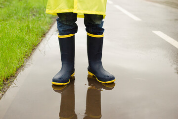 children's rubber boots close-up on wet road. A pair of small children's rain boots with yellow soles standing on wet road in an outdoor setting